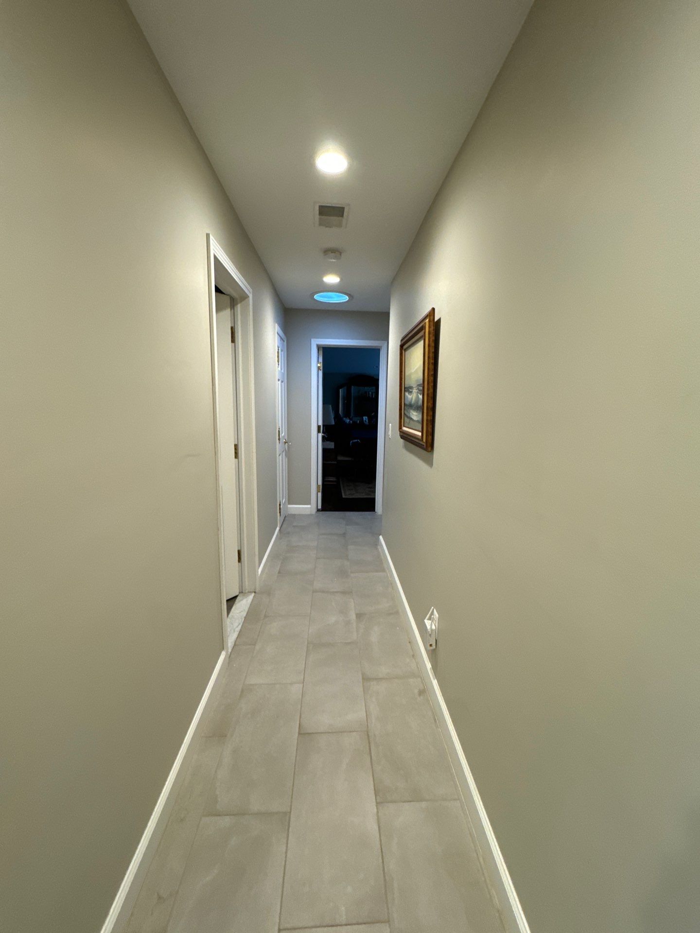 Modern Hallway Interior Painting with Neutral Colors A freshly painted, long, narrow hallway with light gray walls and white baseboards, illuminated by recessed lights.