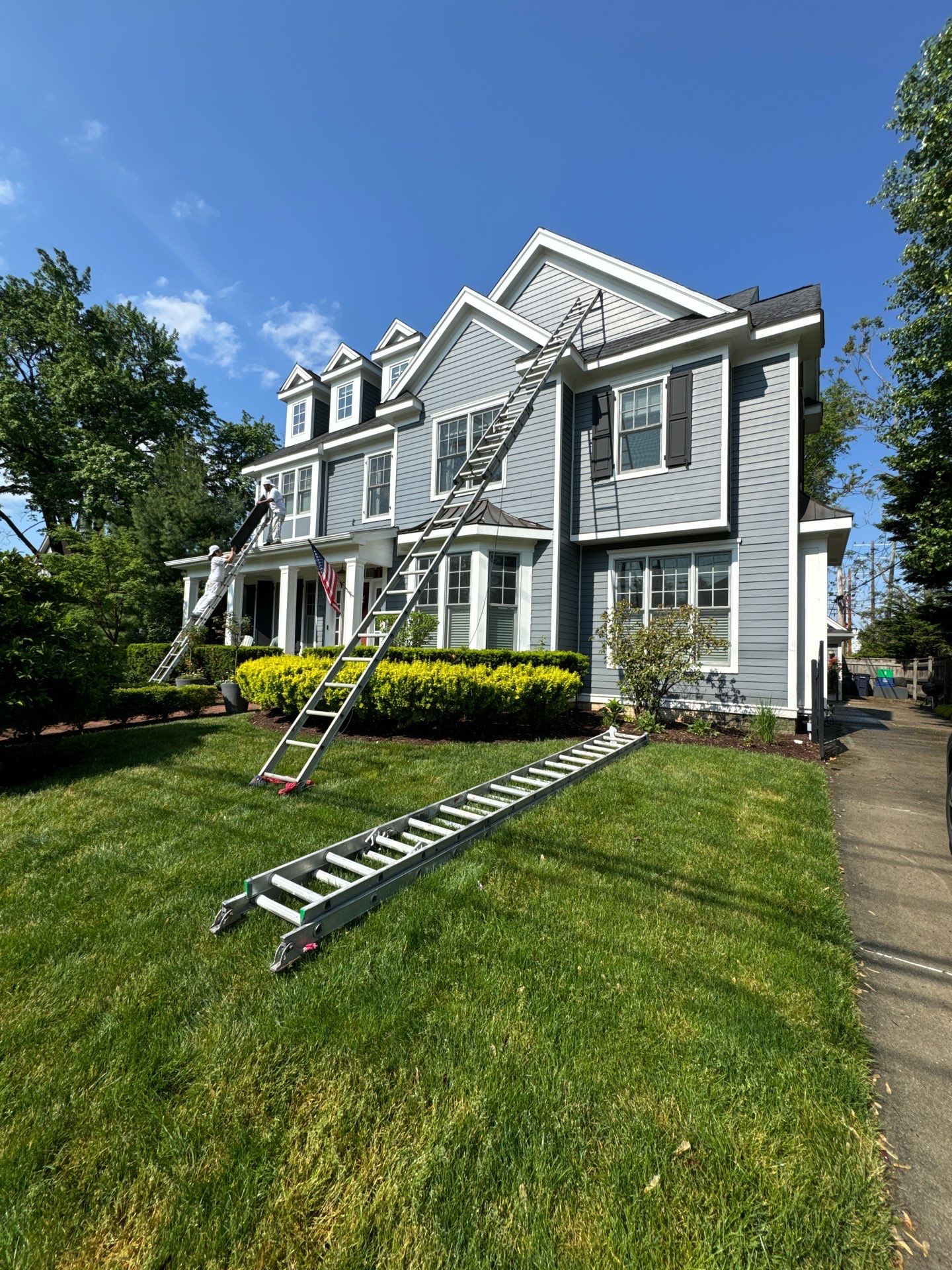 Large Residential Exterior House Painting Project A beautiful two story gray house with white trim, ready for exterior painting with ladders set up.