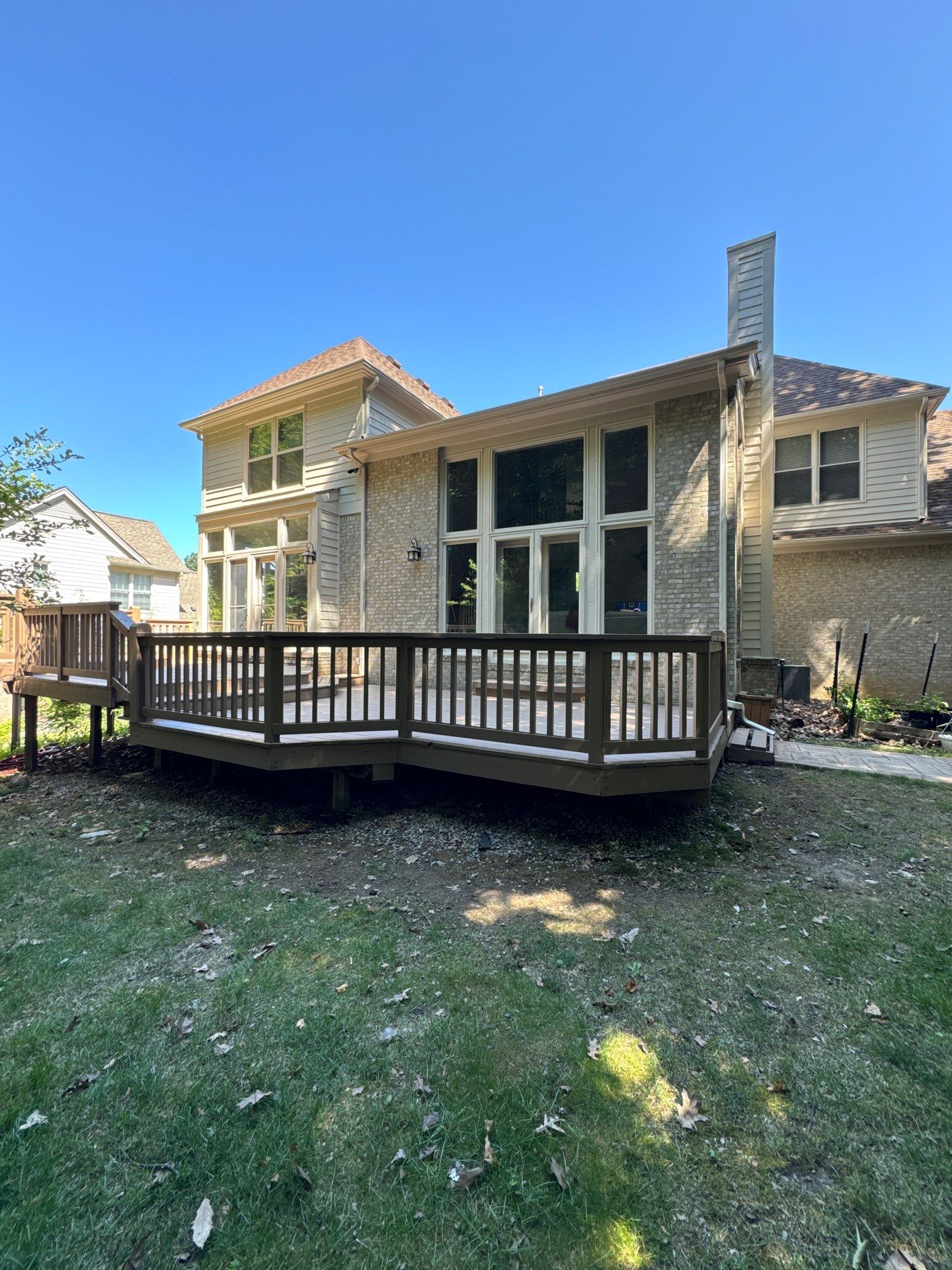 Residential Exterior House Painting and Deck Staining Residential home exterior showcasing light brick, beige siding, and a dark brown stained wooden deck in the backyard.