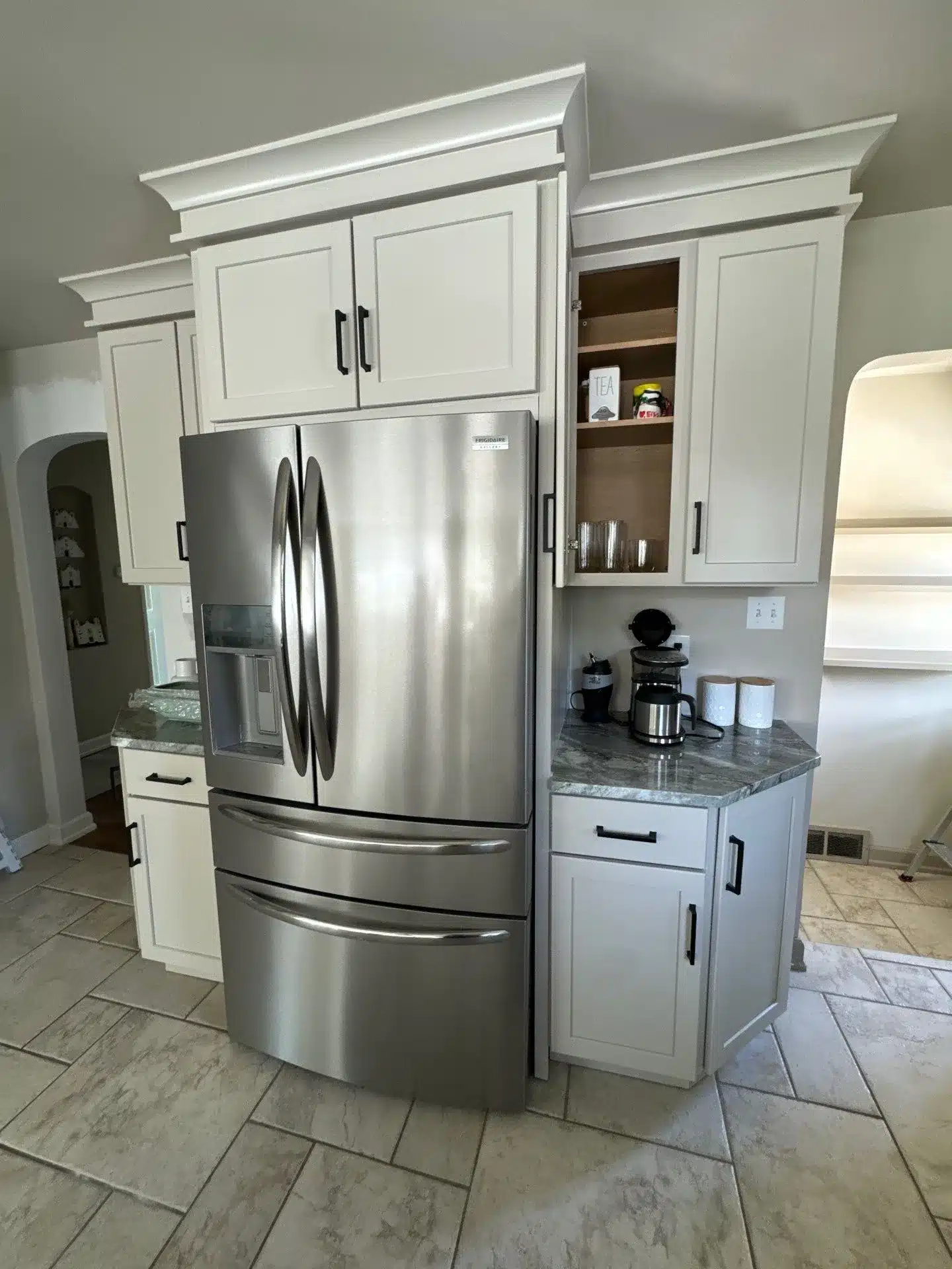 Cream White Painted Kitchen Cabinets Cream-white painted kitchen cabinets with black hardware, decorative crown molding, and open shelving displaying dishware in