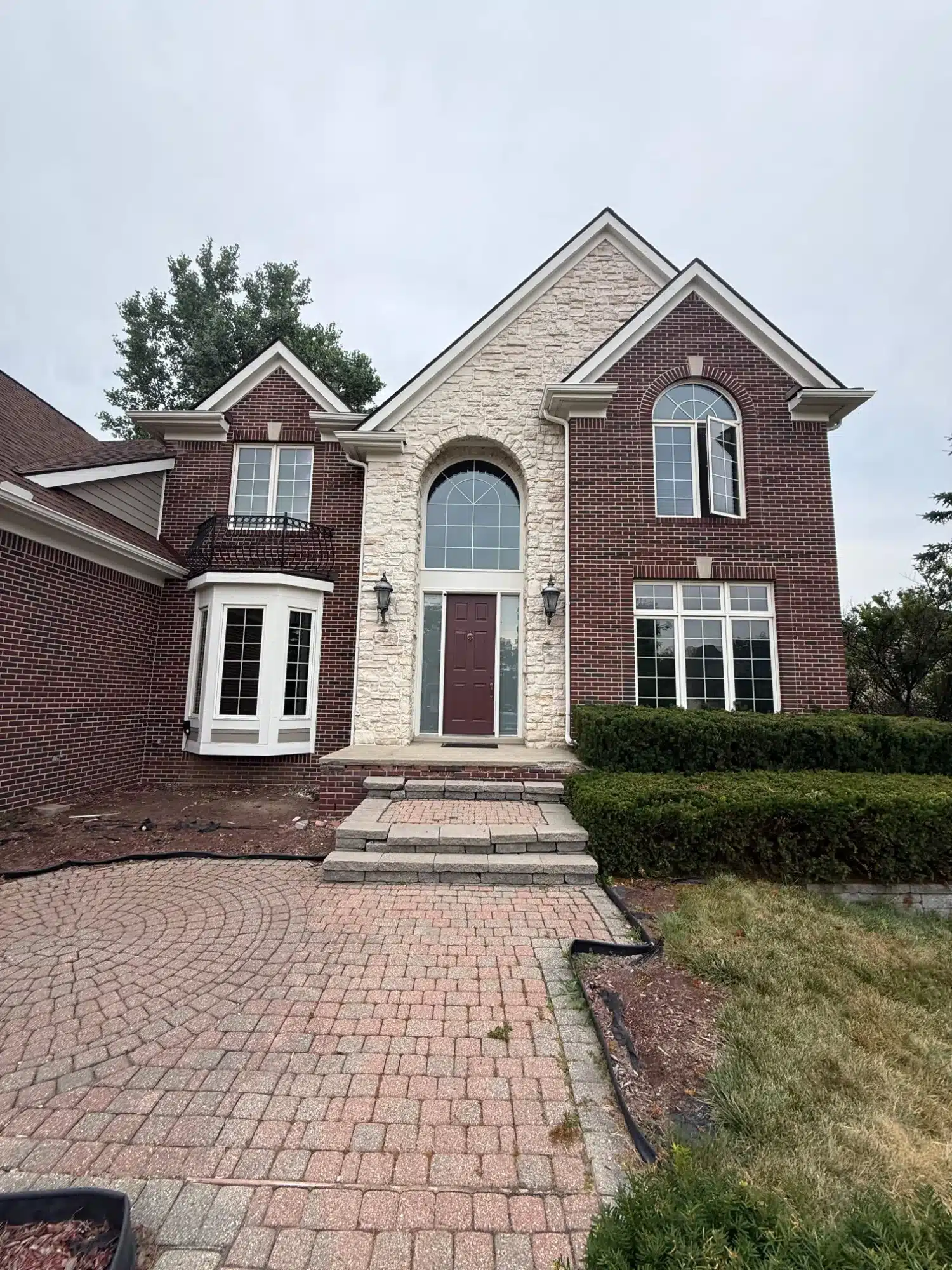 Red Brick and Stone Two-Story Home Red brick two-story residential home with cream stone accent wall, dark burgundy entry door, white-trimmed arched windows