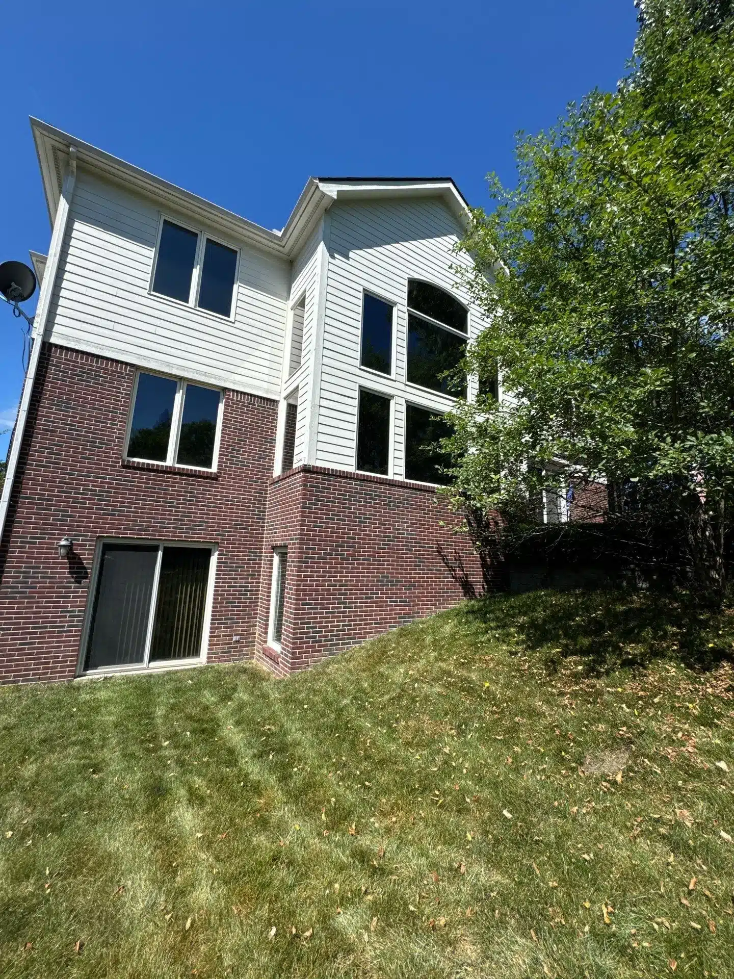 White Siding Brick Home Exterior White horizontal vinyl siding upper section on two-story home with red brick lower level and dark-trimmed windows in